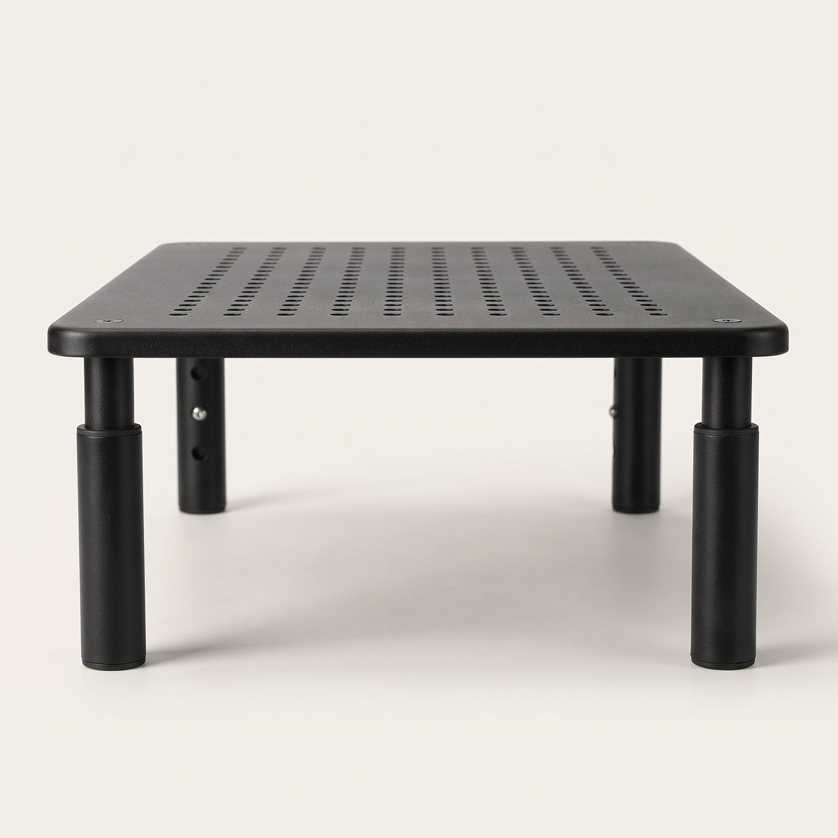 Monitor riser from a low angle, showing the height-adjustable legs and the ventilation holes