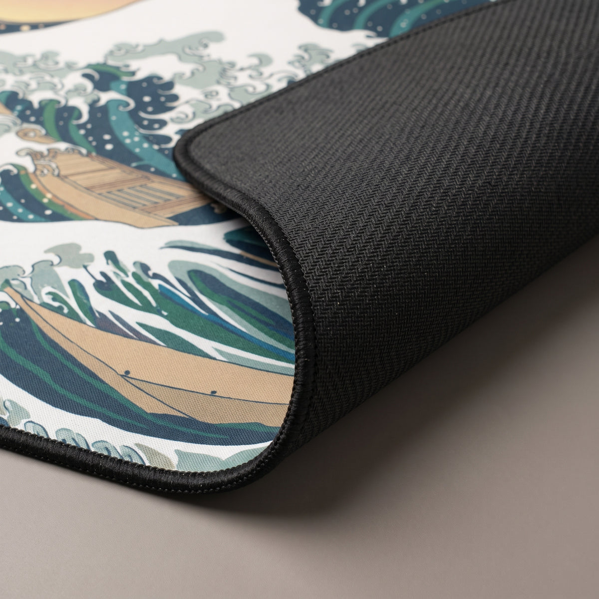 Corner of the Great Wave desk mat lifted to show the stitched edge and natural rubber base