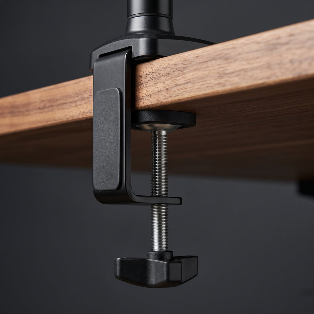 The monitor arm's C-clamp gripping the rear edge of a walnut desktop