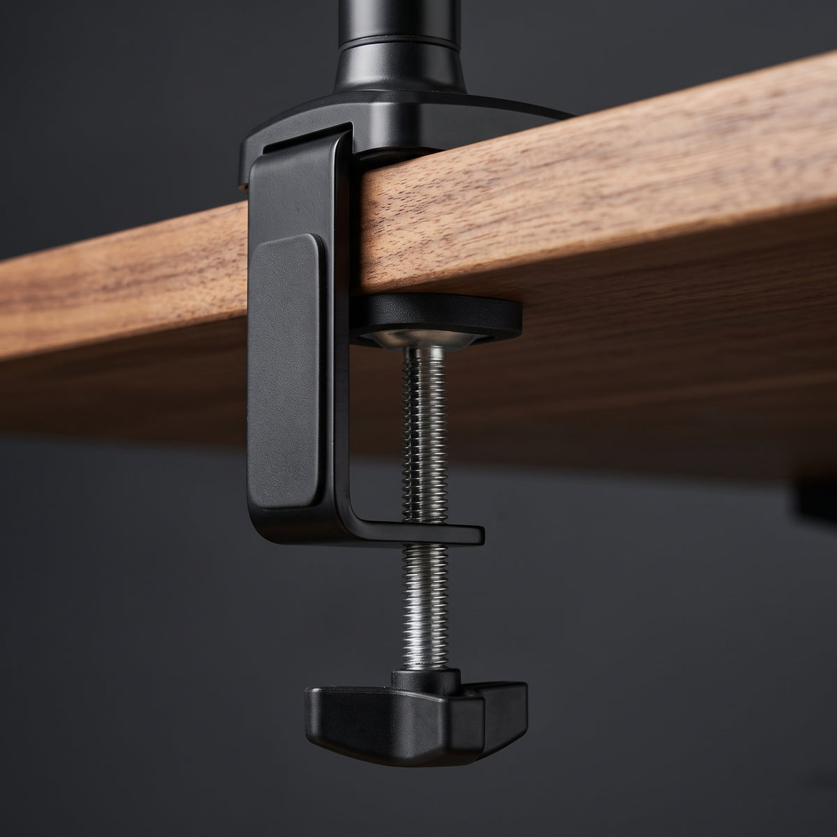 The monitor arm's C-clamp gripping the rear edge of a walnut desktop